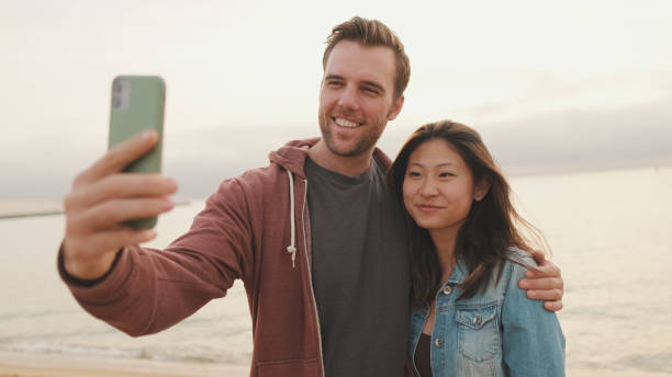 istock Couple in love hugging each other makes selfie while standing on the beach 1456353912