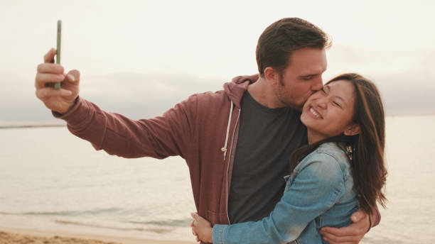 istock Couple in love hugging each other makes selfie while standing on the beach 1456353913