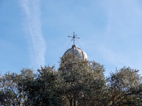 Orthodox chirch dome with cross above green trees crowns under clear blue sky