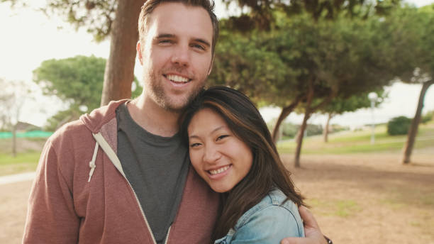 istock Close up, laughing couple hugging each other while standing in the park. looking at camera 1456354046