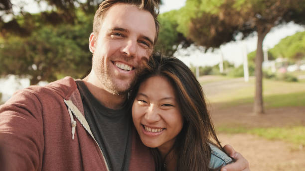 istock Close up, laughing couple hugging each other while standing in the park. looking at camera 1456354047