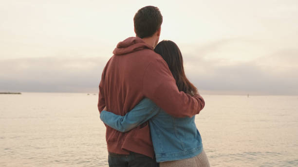 istock Young couple standing embracing on seascape background. Back view 1456354075