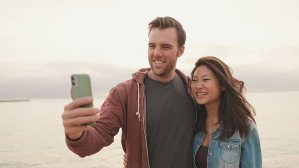 istock Couple in love hugging each other makes selfie while standing on the beach 1456354100