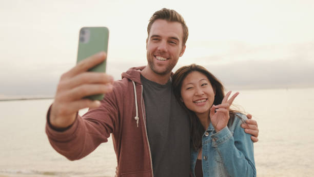 istock Couple in love hugging each other makes selfie while standing on the beach 1456354102