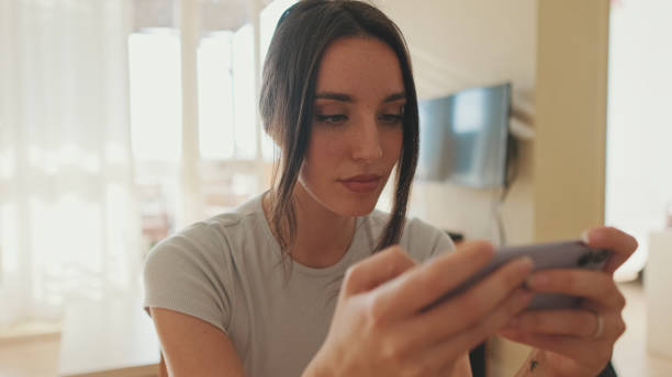 istock Young woman using mobile phone while sitting in apartment 1456355297