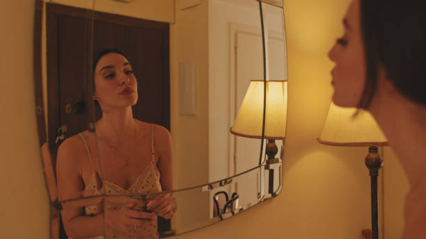 istock Close up, young woman putting on makeup while standing in front of mirror 1456355615