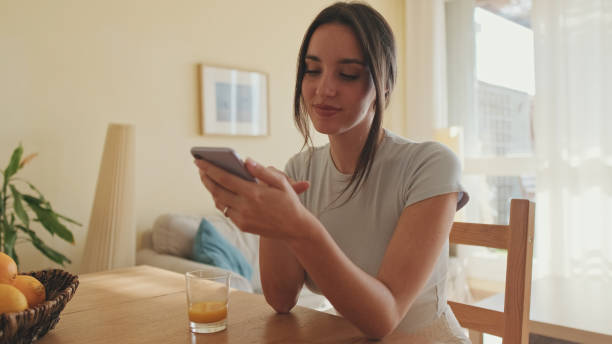 istock Smiling young woman scrolling through photo on her mobile phone while sitting in the kitchen 1456355620