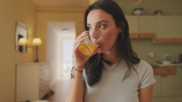 istock Close up, young woman drinking orange juice while sitting in the kitchen 1456355649