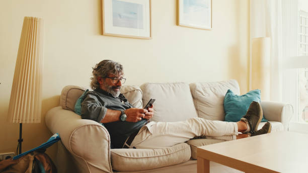 istock Middle-aged man relaxing on his couch while in home and using his smartphone to text 1456355759