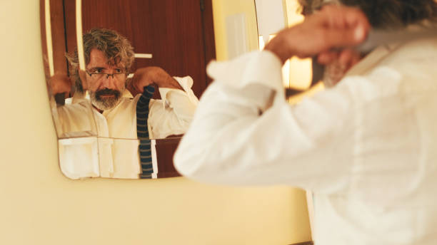 istock Middle-aged man putting on tie while standing in front of mirror 1456355892