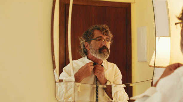istock Middle-aged man putting on tie while standing in front of mirror 1456355900