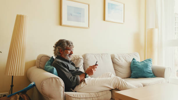 istock Middle-aged man relaxing on his couch while in home and using his smartphone to text 1456355981