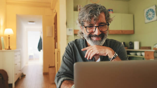 istock Senior working on laptop sitting in home kitchen 1456355987