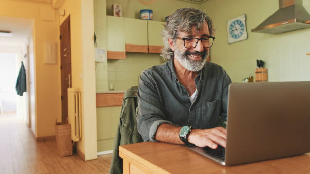 istock Senior working on laptop sitting in home kitchen 1456355988