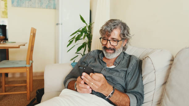 istock Middle-aged man relaxing on his couch while in home and using his smartphone to text 1456355998