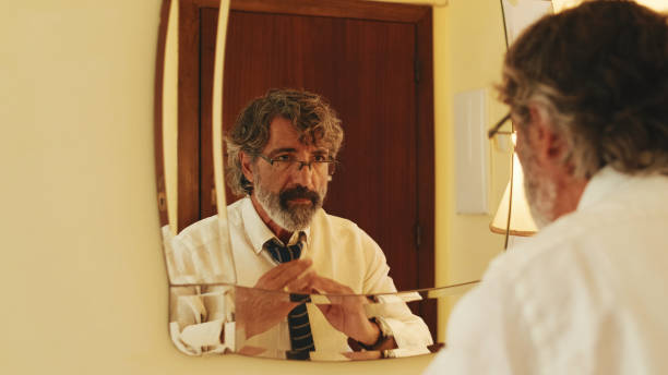 istock Middle-aged man putting on tie while standing in front of mirror 1456356180