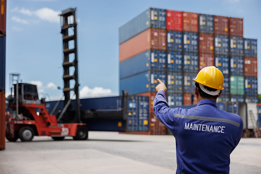 the back side of maintenance worker using walky talky comunicate with lifting operation team with blue sky. Logistics transportation industry forklift handling container box loading stacker.