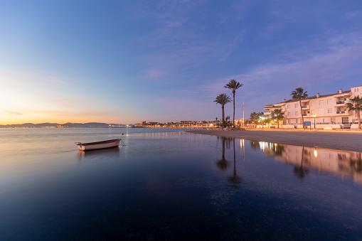View of the Espejo beach in Los Alcazares, Region of Murcia, Spain, at sunrise and with a boat and palm trees in the background