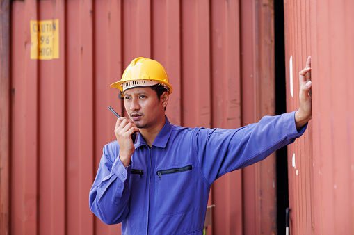 the asian worker is using walky talky comunicate with lifting container team. Logistics transportation industry concept.