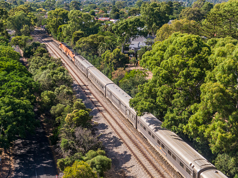 Hawthorn, Australia - Jan 13, 2023: Aerial view of summer urban scene with two special orange diesel locomotives hauling Journey Beyond Rail's Great Southern luxury tourist train, past leafy suburbs in Adelaide's foothills.