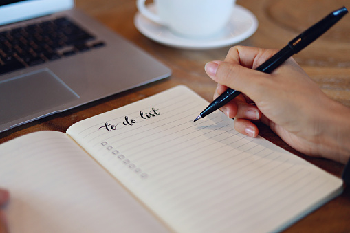 Bolígrafo sostenido, planeando hacer una lista en un cuaderno, computadora portátil y taza de café en el escritorio de la oficina photo