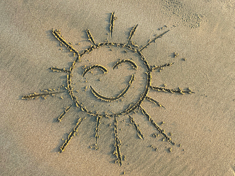 Stock photo showing close-up, elevated view of a sun shape drawn in sand on a sunny beach with a stick. Vacation and holidaying concept.