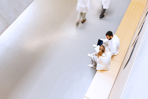 Multi-racial group of chemistry students in white uniforms during lectures in university corridors while casually chatting. View from above. Blurred figures in motion.