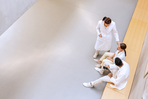 Multi-racial group of chemistry students in white uniforms during lectures in university corridors while casually chatting. View from above.