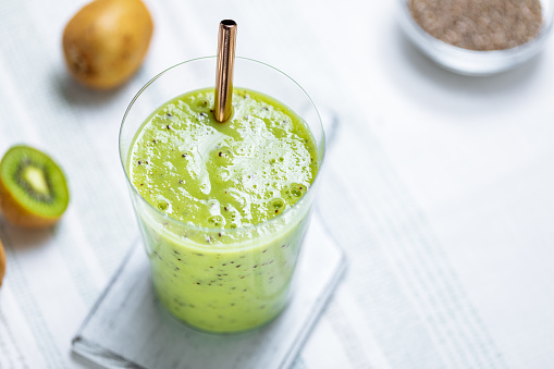 A glass of Green Kiwi Avocado Smoothie Drink with a straw in bright scene