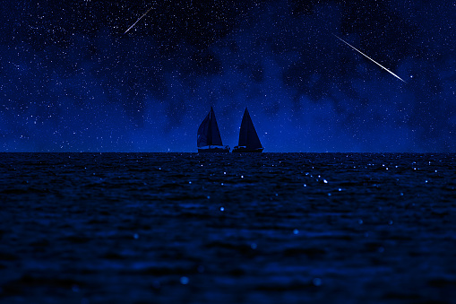 Sailing boat silhouette with starry Milky Way skies above open ocean waters.
