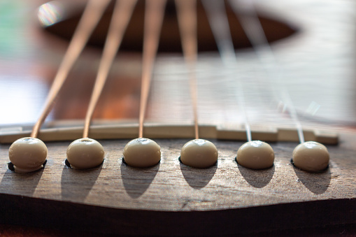 Acoustic guitar bridge with one pins and strings close up with selective shallow focus.
