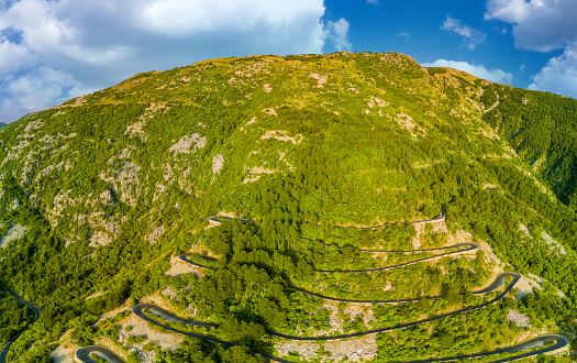 Panorama of incredible winding mountain road - Lovcensky serpentine with dangerous sharp extreme turns that leads to top of mountain range of the Montenegrin mountains covered with green vegetation