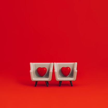 Creative 70s or 80s retro fashion aesthetic love concept. Minimal romantic idea. Two red heart in gray armchairs against vivid red background. Love or Valentine's Day composition.