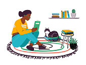istock Woman reading book at home. Young female character sitting on carpet with textbook. Student girl wearing glasses preparing for exams 1456379080