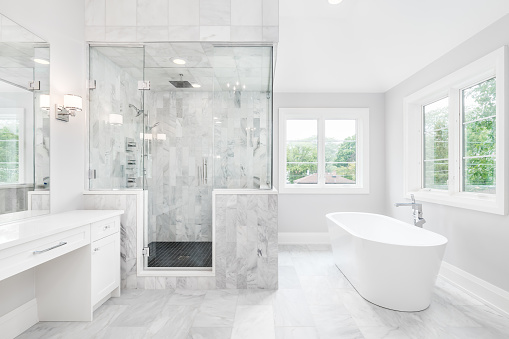 A large luxurious bathroom with a stand alone tub, white vanity, and a glass stand up shower with marble tiles and bench seat.
