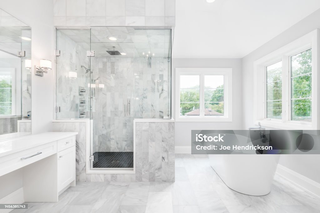 A luxury bathroom with a walk-in tiled shower and standalone tub. A large luxurious bathroom with a stand alone tub, white vanity, and a glass stand up shower with marble tiles and bench seat. Bathroom Stock Photo