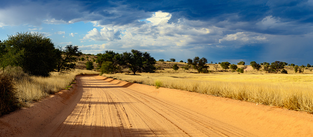 View of thunder clouds over desert track through Kalahari desert