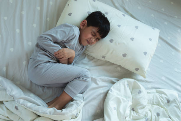 Top View of Asian boy lying in bed with stomach ache Top View of Asian boy lying in bed with stomach ache. Sick little child in bedroom at home. Diarrhea and illness in children diarrhea stock pictures, royalty-free photos & images