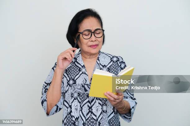 Elderly Asian Woman Thinking Something When Reading A Book Stock Photo - Download Image Now