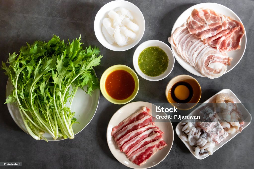 Hot pot set seafood, meat sliced, shirataki noodles with mizuna  vegetable. Delicious shabu at home; top view on black table background. Ingredient Stock Photo