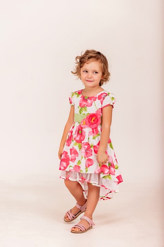 Stylish 4-5 year old little girl in sundress on white background looks at camera. Concept Birthday and Children Celebration. Adorable child in flowers dress posing and showing emotions. Copy space