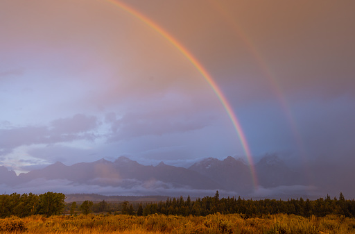 a scenic landscape in the Tetons in autumn with a rainbow and storm clouds