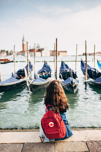 Student with backpack enjoying the view of venice when sitting on the ground in front of the gondolas