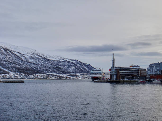 Tromso, Norway - 03 13 2013: Hurtig Routes post and cruise ship in the winter landscape of the port of Tromso in a fjord at the coastline of northern Norway with snow covered mountains in the background