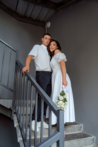 Bride and groom stand on the stairs, portrait of the newlyweds, a bride with a bouquet of white flowers. Valentine's Day