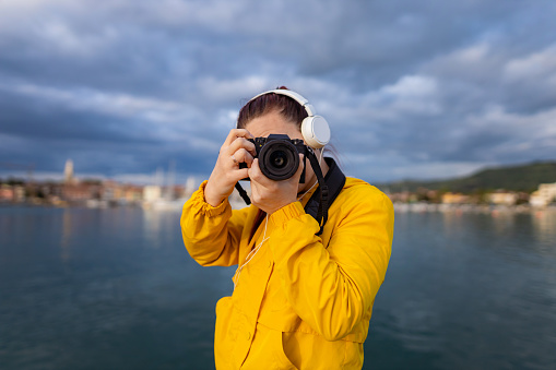 A front view of one young female photographer with headphones holding the camera and capturing the view.