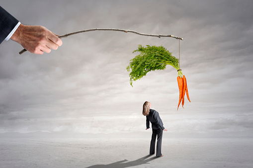 A woman looks up as a man dangles a carrot from a stick.