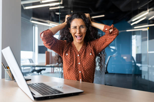 Angry businesswoman yelling at camera, latin american woman holding her head angry working inside modern office using laptop at work Angry businesswoman yelling at camera, latin american woman holding her head angry working inside modern office using laptop at work. nettle stock pictures, royalty-free photos & images