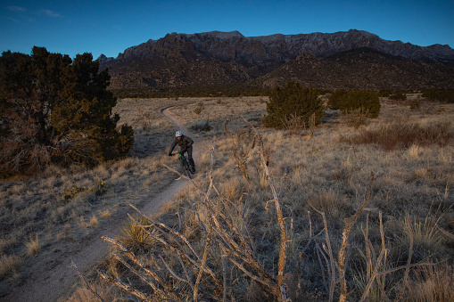 a man makes his way across the landscape at sunset while riding his mountain bike.  such beautiful nature scenery and adventure and exercise opportunities abound in central new mexico.