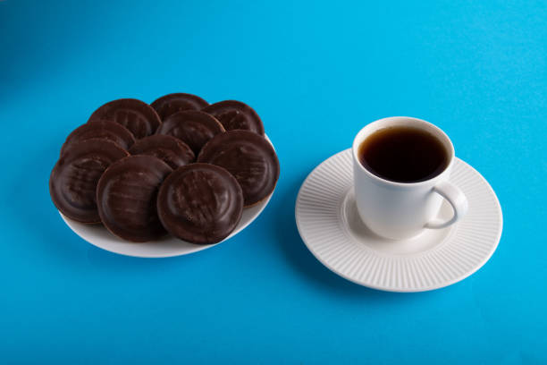 biscotti con gocce di cioccolato fotografico su un piatto bianco e una tazza di tè su un piattino - biscotti cookie morning temptation foto e immagini stock